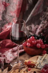 Glass of red wine served with blue cheese on dark wooden background. Autumn picnic with wine and cheese platter, fruits and dry leaves in rustic style