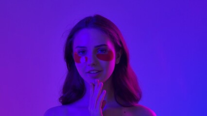 Young woman posing at camera puts an eyepatches under eyes, isolated on blue neon background. Natural beauty and skin care concept