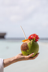 tropical refreshing coconut cocktail in female hands, ocean in the background, paradise