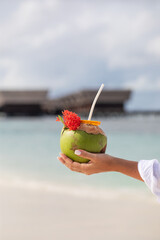 tropical refreshing coconut cocktail in female hands, ocean in the background, paradise