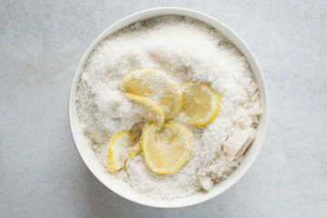 Overhead view of lemon slices and sugar being mixed together in a white bowl, process of making lemon cheong or lemon syrup
