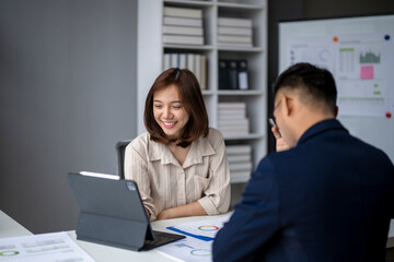 Fototapeta premium A woman and a man are sitting at a desk with a laptop and a tablet