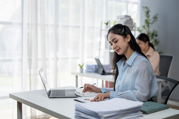 A woman is sitting at a desk with a laptop and a stack of papers