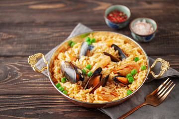 Traditional spanish seafood paella with rice, mussels, shrimps in a pan on wooden background.