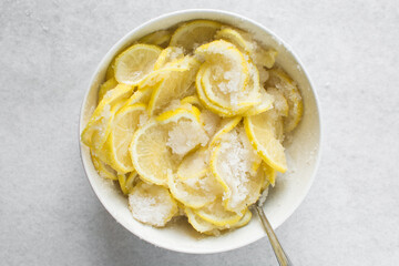 Overhead view of lemon slices and sugar being mixed together in a white bowl, process of making lemon cheong or lemon syrup