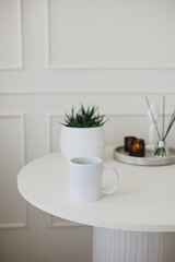 Still life with white mug, aromatic sticks and candles on a table in a cozy living room.