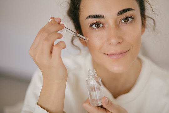 Young woman 30 years old applying face oil on her skin.