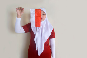 Young Asian Muslim Woman Holding Little Indonesia Flag To Covering Her Half Face. Indonesian Independence Day Celebration