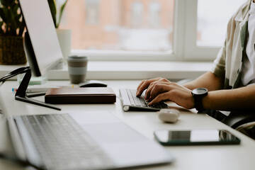 Medium close up of unrecognizable male hands with black watch typing on black keyboard in light office