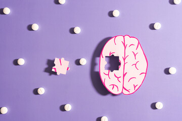 Human brain anatomy missing a piece of jigsaw puzzle with medicine pills on purple background. Treatment of Alzheimer's disease, Dementia and Parkinson disease concept. Mental health care.