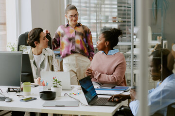 Biracial colleagues chatting in office while their african american coworker using laptop to write codes
