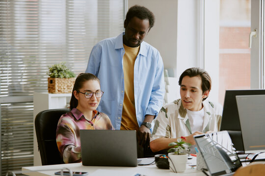 African American teamlead standing between two Caucasian coworkers who showing new project to him - Powered by Adobe