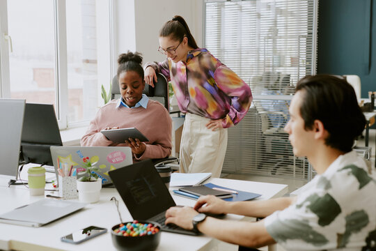 Biracial female coworkers having discussion and looking at touchpad while male programmer writing codes