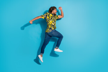 Full size photo of crazy funky man dressed print shirt jeans jumping run look at offer empty space isolated on blue color background