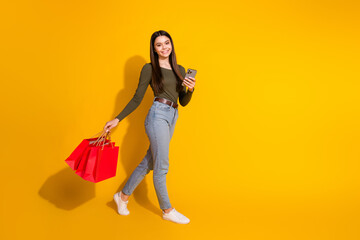 Full size photo of pretty teenager girl walk shopping bags device wear trendy khaki outfit isolated on yellow color background