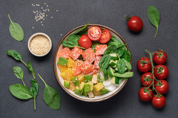 Salmon bowl with spinach, rice, avocado, tomato, cucumbers on black background, top view. Poke bowl, healthy eating