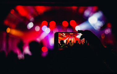 person filming with cellphone a festival in the background