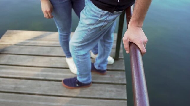 A couple is framed by a walkway pole by the river, as the water flows slowly by. The scene captures a tranquil and romantic moment in nature, highlighting the beauty of the riverside on a sunny day