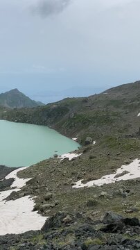 Lac blanc vu de haut, entour&eacute; par une montagne dont la pente est &agrave; moiti&eacute; enneig&eacute;e. La neige contraste avec les parties d&eacute;nud&eacute;es, cr&eacute;ant un paysage alpin spectaculaire et glac&eacute;.