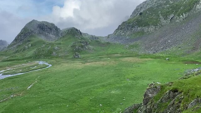 Une petite rivi&egrave;re serpente &agrave; travers une plaine de montagne, entour&eacute;e de sommets majestueux. L'eau scintille sous le ciel clair, offrant un contraste paisible avec les montagnes environnantes.