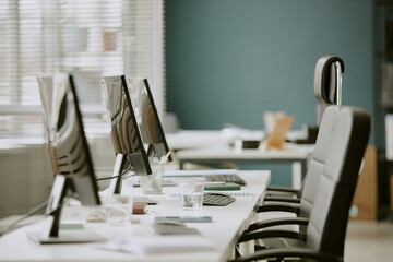 Work zone fully equipped with white wooden table with black computers and office supplies on top in spacious modern office