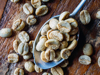 Top view green coffee bean on a stainless steel spoon, Close-up of fresh raw coffee bean, unroasted  coffee bean on wooden table, macro