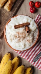 Corn hominy with cinnamon in ceramic bowl, bananas, acerola and cassava in the wood background....