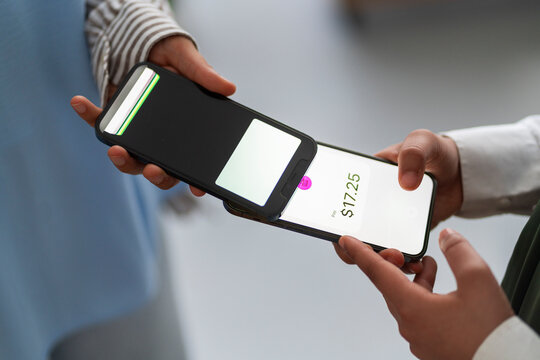 Close-up of two people using their mobile phones for tap to pay contactless payment One phone displays the amount to be paid, showing a modern and convenient transaction method - Powered by Adobe