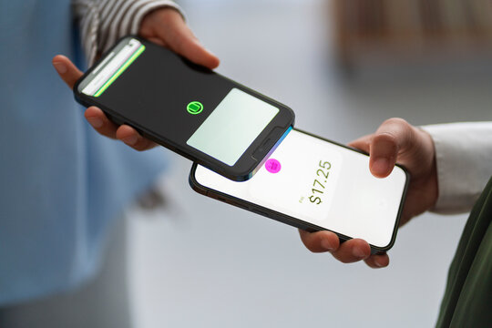 Close-up of two people using their mobile phones for tap to pay contactless payment One phone displays the amount to be paid, showing a modern and convenient transaction method