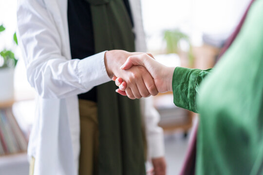 A close-up shot of two women shaking hands in an office setting The focus is on their hands, symbolizing agreement, partnership, and mutual respect