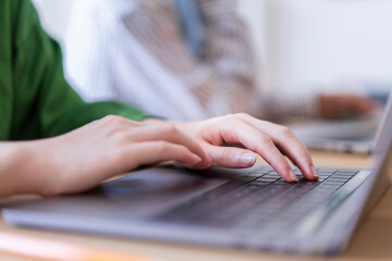 Close-up of a woman's hands typing on a laptop in a modern office setting The focus is on her hands and the technology used for work