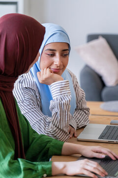 Two women in hijabs work intently on a laptop in a modern office environment Their focused expressions highlight their dedication and teamwork