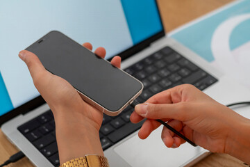 A close-up of hands connecting a smartphone to a laptop using a cable. This image highlights the integration of technology and seamless data transfer in a modern workspace.