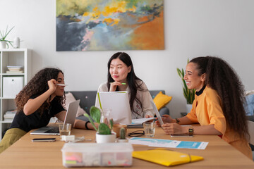 Three young professionals collaborating creatively during a meeting, using laptops and tablets in a vibrant office setting, actively exchanging ideas and solutions