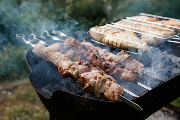 Close up of delicious fragrant grilled pork slices planted on skewers on a barbecue with hot coals. Space for text