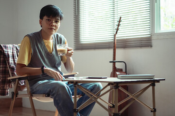 Fototapeta premium Asian embracing LGBTQ identities, smile warmly at the camera, enjoying coffee and guitar near window capturing a joyful and inclusive moment of their lifestyle at home.
