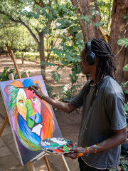 African painter painting a colorful lion standing on a park