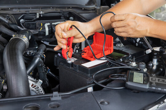 Man is measuring AGM battery power of suv car by battery tester at home.