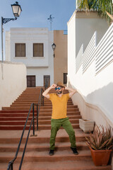 Young Hispanic man adjusting his hat and posing on a ladder in the street