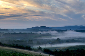 Landscape with backlit clouds and mists over the hills just after sunrise