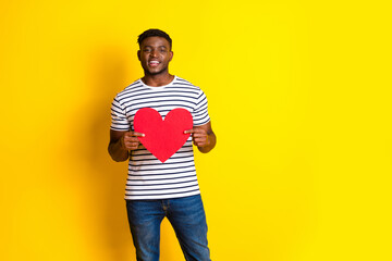 Naklejka premium Portrait of nice young man heart symbol card empty space wear striped t-shirt isolated on vibrant yellow color background