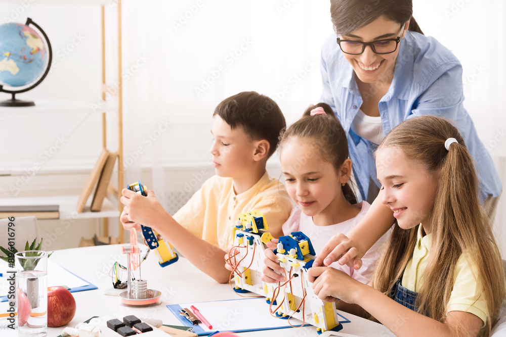 Leinwandbilder A group of elementary school students are working on a robotics project in a classroom setting. They are building robots with the help of their teacher, who is smiling and guiding them.