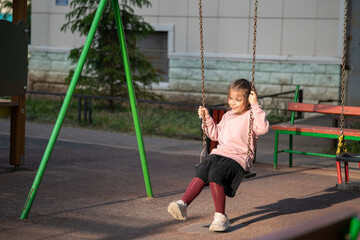 A seven-year-old girl sits on a swing in the yard. High quality photo