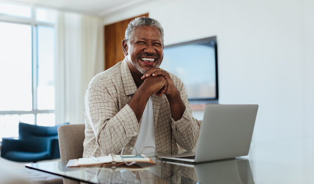 Cheerful senior man working on laptop at home office with bright smile