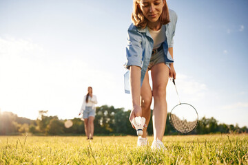 Picking up the fallen shuttlecock. Two women are having fun, with badminton rackets, on the field