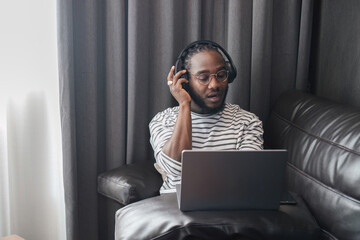Young African American Man Wearing Headphones and Working on Laptop in Modern Living Room