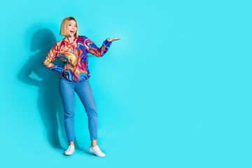 Full size photo of impressed cute girl dressed print shirt jeans arm demonstrate product empty space isolated on blue color background