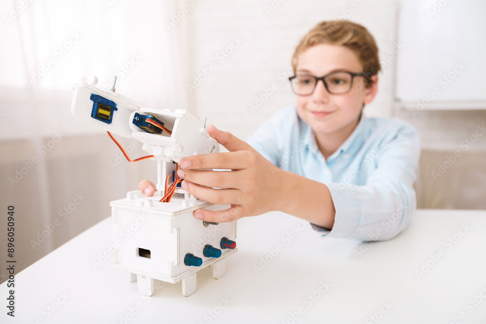 Poster a young boy wearing glasses is seen at a desk, focused on assembling a white robotic arm model. he c
