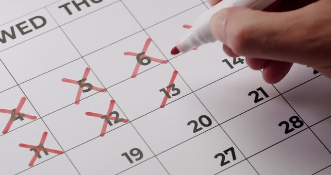 Close-up image of a hand marking off days on a calendar with a red marker, representing progress, schedule, time management, and countdown. Hand Crossing Off Days On Calendar With Red Marker