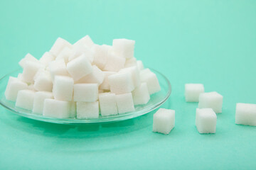 White sugar cubes on glass plate on green background, sweet food ingredient